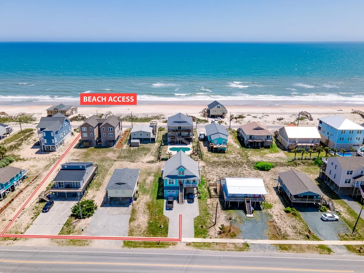 This image captures a beach access sign with a glimpse of the ocean and surrounding homes, inviting viewers to imagine easy strolls to the beach. The open, inviting pathway clearly signals proximity to the shoreline and the relaxed, pet-friendly nature of the area.