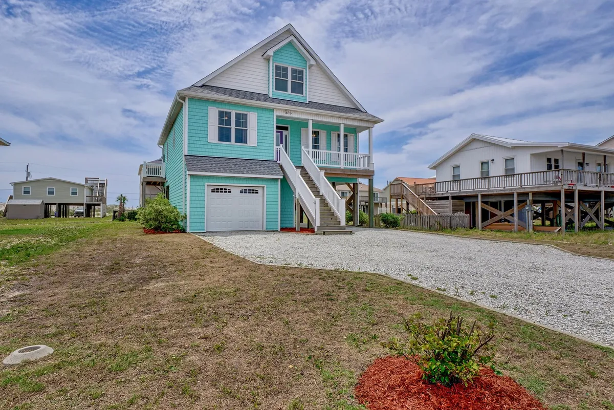 This image features the turquoise exterior of the house, a welcoming stairway leading up to the entrance, and a spacious driveway. The porch is visible, hinting at a sociable outdoor space, while the driveway underscores ample parking. The cheerful mood and visible yard align with group gatherings and outdoor celebrations.