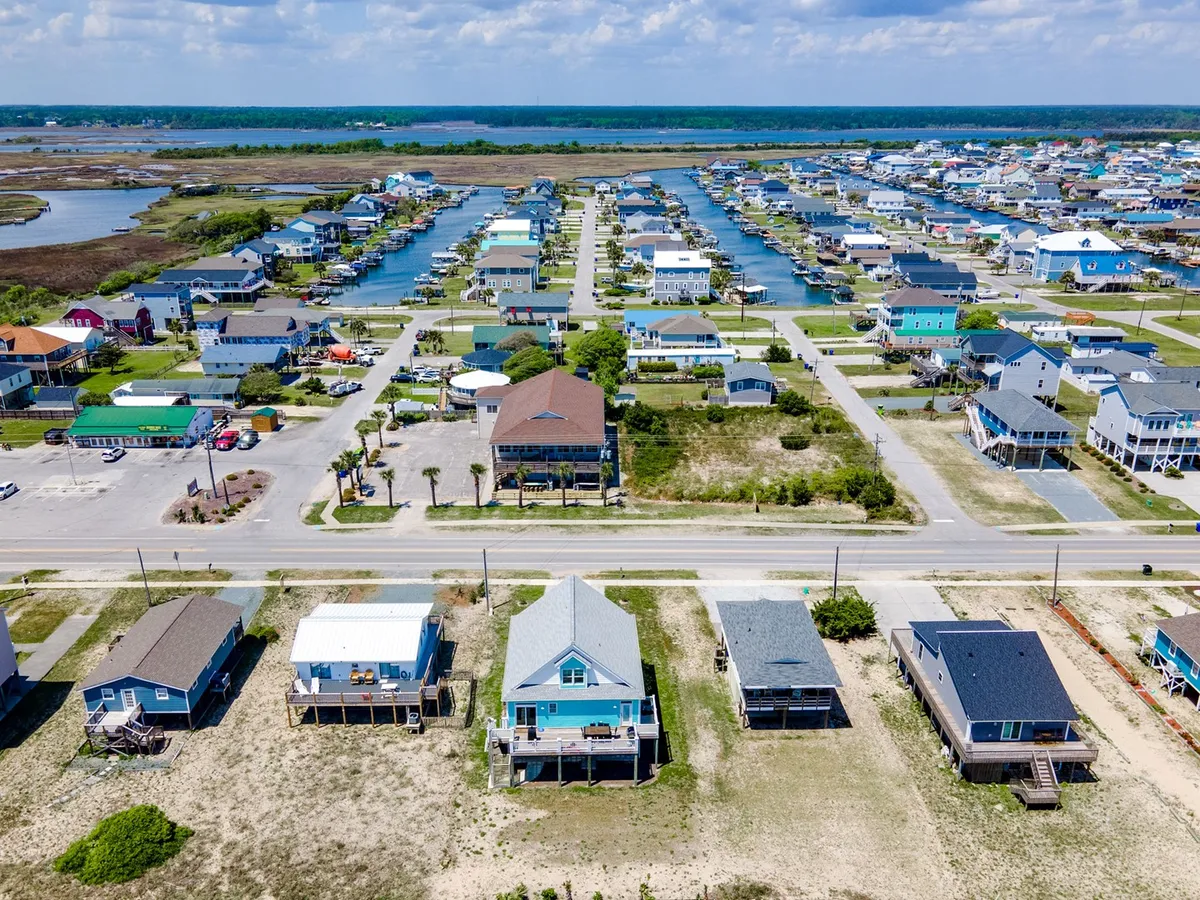 An aerial view showcasing colorful houses, waterways with canals, green spaces, and roadways. The scene conveys a relaxed coastal neighborhood, perfect for kayaking and paddleboarding, with abundant opportunities for outdoor exploration.