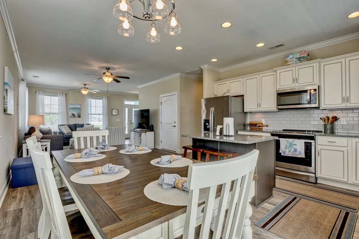 Inside, a spacious open-concept area features a large dining table set for a meal, a kitchen island, and a comfortable living space with a sofa. The layout is perfect for communal meals, game nights, and group relaxation, with plenty of space for everyone to gather together.